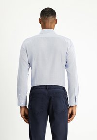 Camicia a righe blu chiaro con maniche lunghe, polsini con bottoni e colletto, indossata con pantaloni blu navy dotati di vita elasticizzata.