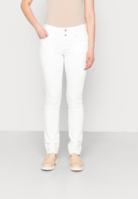 Jeans blancos ajustados con una textura suave, con una cintura de altura media y dos bolsillos delanteros. Combinados con zapatos beige de tipo slip-on.