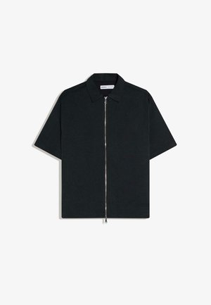 Chemise noire à manches courtes avec un col et une fermeture éclair argentée sur toute la longueur à l'avant, posée à plat sur un fond blanc.