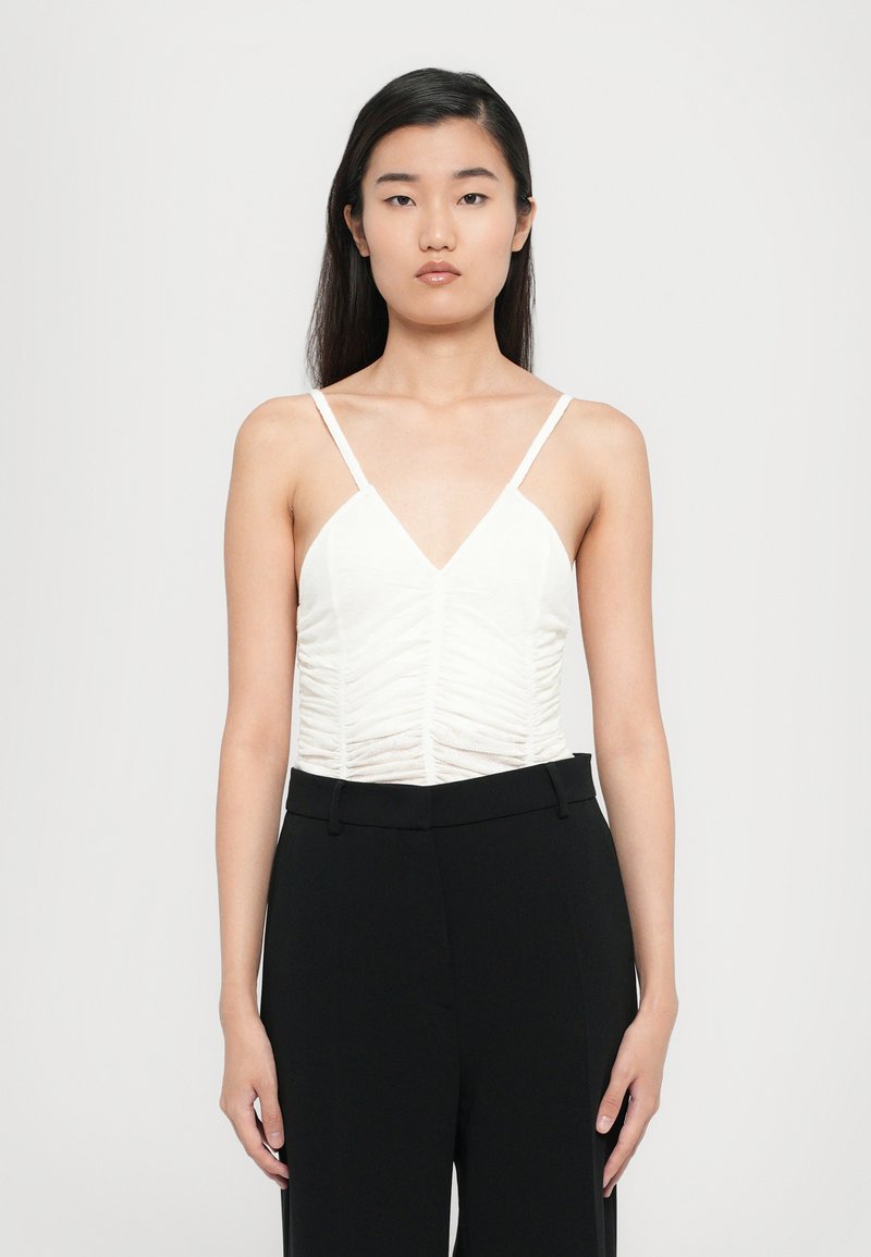 Haut blanc sans manches avec un col en V et une texture froncée, associé à un pantalon noir à taille haute. Design simple avec des bretelles fines.