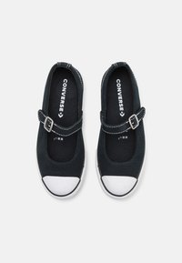 Zapatos Mary Jane de lienzo negro con puntera de goma blanca, correa con hebilla y costuras blancas contrastantes en la parte superior. Suela plana.