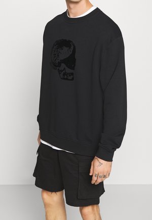 Sort sweatshirt med en tekstureret kraniegrafik, rund halsudskæring og lange ærmer. Matcher med sorte cargo-short.
