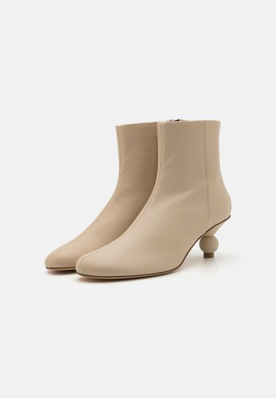 Boots de piele bej la glezne cu vârful ascuțit, închidere cu fermoar pe lateral și un design unic al tocului rotund. Textură netedă și stil minimalist.