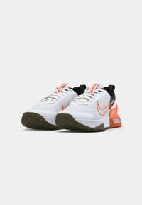 Baskets blanches de sport avec une tige en mesh, des accents orange, un contrefort de talon noir et une semelle en caoutchouc texturé. Comprend un système de laçage et une marque.