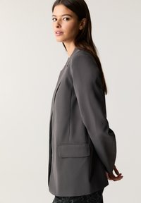 Grau taillierter Blazer mit Reverskragen, Ein-Knopf-Verschluss und seitlichen Taschen, gefertigt aus glattem Stoff mit einer schlanken Silhouette.