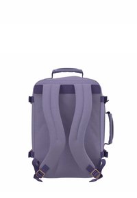 Zaino in tessuto viola con due spallacci imbottiti, un manico superiore e cinturini laterali regolabili. Design minimalista senza motivi visibili.