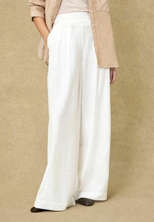 White wide-leg trousers with a textured finish, featuring side pockets and a high waistband, paired with a striped beige blouse.