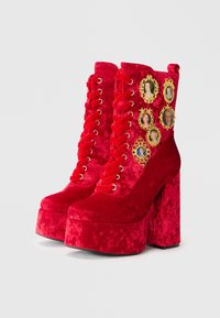 Bottes de cheville en velours rouge à plateforme avec des embellissements de portraits encadrés en or, un design à lacets et un talon carré épais.