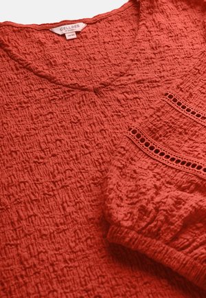 Rode blouse met textuur, elastische manchetten en decoratieve horizontale uitsnijdingen, gelabeld "Cellbes of Sweden", maat 38/40.
