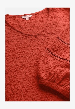 Rode blouse met textuur, elastische manchetten en decoratieve horizontale uitsnijdingen, gelabeld "Cellbes of Sweden", maat 38/40.