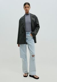 Overmaatse grijze blazer met een subtiel patroon, gecombineerd met een aansluitend grijs topje en lichtblauwe ripped jeans. Zwarte slippers maken de look compleet.