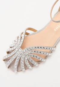 Sandale argintii de seară cu un design decorativ ce include pietre strass și bretele încrucișate. Captuseala interioară netedă și forma cu vârf deschis.