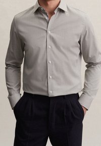 Grå knapp-up skjorta med en subtil textur, spetsig krage och vita knappar. Bärs med mörka veckade byxor.