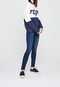 Marinblå, rosa och vit färgblockerad sweatshirt med "PEPE"-logotyp, kombinerad med slim-fit mörka jeans och svarta kanvas sneakers.