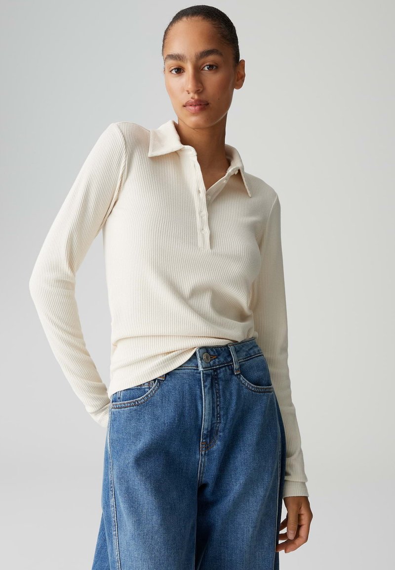 Polo a maniche lunghe color crema a coste con bottoni, abbinata a jeans di denim blu a vita alta. Tessuto liscio e design classico con colletto.