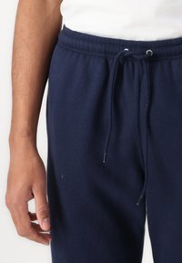 Calças de fato de treino azul-marinho feitas de tecido macio, com cintura elástica, cordões ajustáveis e pontas em metal.