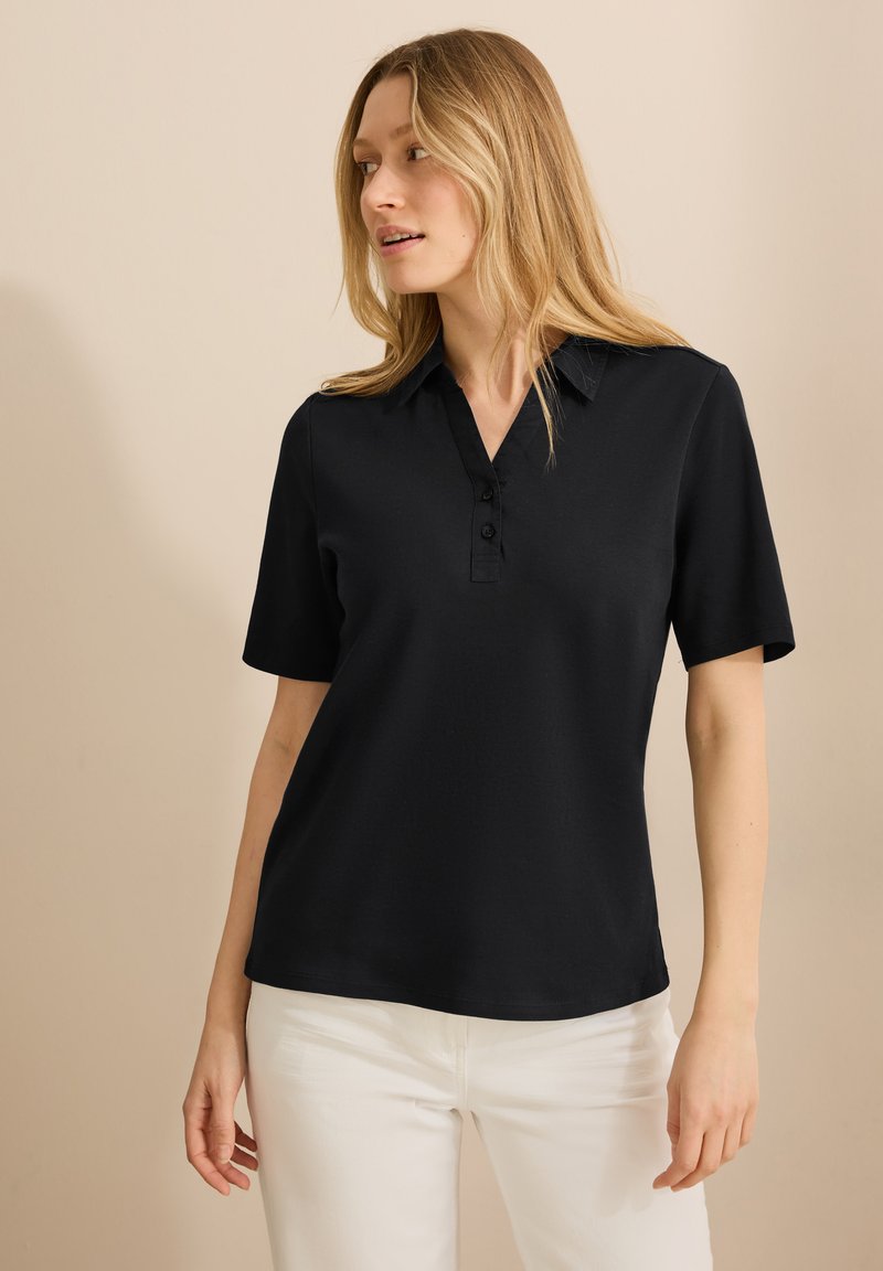 Zwarte polo met korte mouwen, een V-hals, een drieknoopsbies en een gladde, lichte stof, gecombineerd met witte broek.