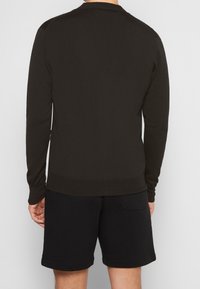 Mörkgrön stickad tröja med lång ärm, rund hals, ribbade mudd och nederkant, i kombination med svarta shorts. Texturen verkar slät och åtsittande.