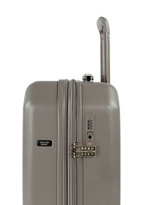 Maleta rígida gris con doble cremallera, cerradura combinada incorporada y asa retráctil. Presenta la marca DKNY y acabado brillante.