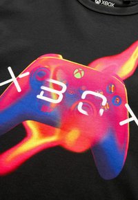 Černé tričko se světlou grafikou ovladače Xbox, zobrazující živé růžové, fialové a modré odstíny s výraznými tlačítky a akcenty.