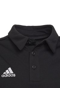Czarny polo z teksturowanej tkaniny, z klasycznym kołnierzykiem, trzema guzikami oraz białym logo Adidas na lewej piersi.