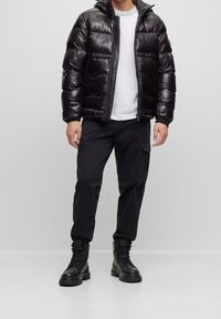 Black padded jacket with a hood, featuring a front zipper and elastic cuffs. Paired with black cargo pants and black lace-up boots.