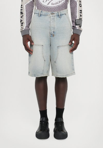 Denim shorts in light blue, featuring front pockets and a raw hem. Paired with black sneakers and black socks.