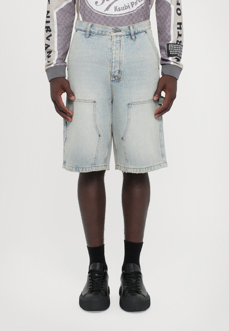 Lichtblauwe denim shorts met voorzakken en een onafgewerkte zoom. Gekleed met zwarte sneakers en zwarte sokken.
