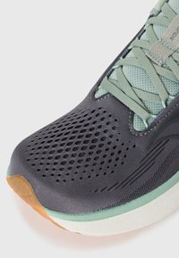 Chaussure de sport avec un upper gris foncé, texture en maille, accents vert menthe et une semelle en caoutchouc beige. Elle dispose de trous de ventilation et de lacets plats.