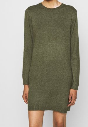 Persona vistiendo un vestido suéter de punto de manga larga color verde oliva con puños y dobladillo acanalados, de pie contra un fondo claro liso.