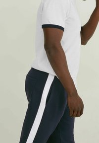 Valkoinen t-paita, jossa on tummansininen reunus, yhdistettynä tummansinisiin collegehousuihin, joissa on valkoiset sivuraitat ja taskut. Sujuva rakenne ja rento malli.