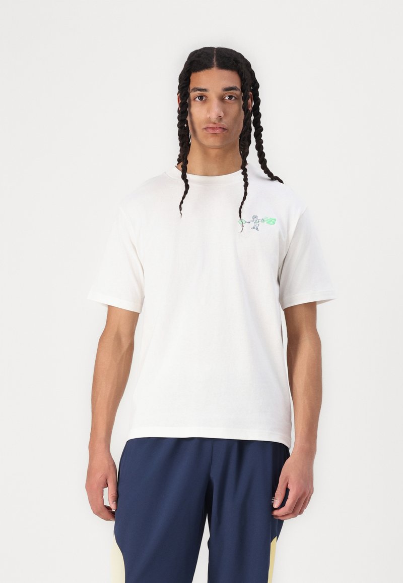 T-shirt en coton blanc à manches courtes, avec un petit graphique coloré sur la poitrine gauche, associé à un pantalon navy.