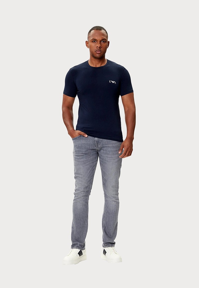 Granatowy bawełniany t-shirt z krótkim rękawem i okrągłym dekoltem, zestawiony z jasnoszarymi dżinsami oraz białymi tenisówkami z czarnymi akcentami.