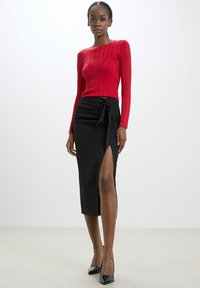 Top rosso a maniche lunghe con righe abbinato a una gonna nera aderente con uno spacco laterale e un dettaglio con fiocco in vita. Scarpe nere con tacco alto.