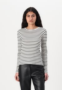 T-shirt à manches longues, en maille côtelée, à rayures horizontales blanches et noires, avec un col rond et une coupe ajustée, porté avec un pantalon en cuir noir.