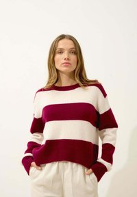 Pull en maille avec des rayures bordeaux et crème audacieuses, col rond et poignets côtelés. Texture chaude, coupe légèrement oversize.