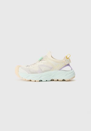 Sneaker leggera con tomaia in rete color crema, accenti verde menta e lavanda, suola spessa azzurro chiaro e un'etichetta gialla sul tallone.