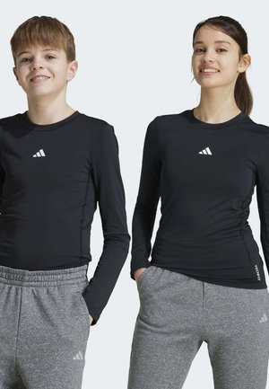 Czarne długie rękawy koszulki sportowe z białym logo, zestawione z szarymi, teksturowanymi dresami. Oba elementy odzieży mają dopasowany krój.