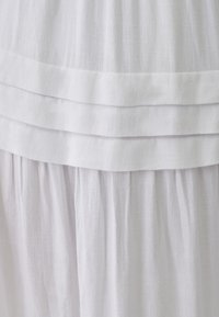 Tela blanca texturizada que presenta un diseño en capas. La parte superior tiene una banda suave y plana con líneas horizontales por encima de una sección inferior recolectada y fluida.