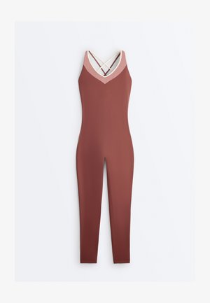 Slim-fit rust-colored jumpsuit with pink V-neck trim and crisscross beige and rust shoulder straps.