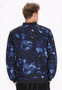Zwart en blauw tie-dye bomberjack met een ribbelkraag en -manchetten, met een zachte textuur en een relaxte pasvorm.