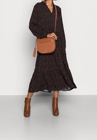 Černé šaty s oranžovými puntíky, dlouhými rukávy a vícevrstvou sukní, doplněné hnědými kotníkovými botami a odpovídající kabelkou přes rameno.