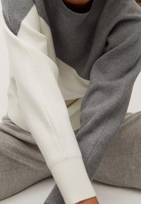 Gray and cream color-blocked sweater with a round neck, textured knit, and ribbed cuffs, paired with gray pants.