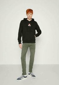 Čierna mikina s kapucňou a červeno-bielym logom "DIESEL", kombinovaná s olivovozelenými nohavicami a modrými teniskami so bielymi pruhmi. Pohodlný strih.