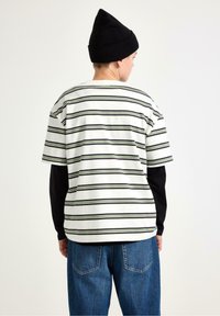 Stripet kortærmet skjorte i hvid med grønne og sorte linjer; båret over en sort langærmet top; kombineret med blå denimjeans.