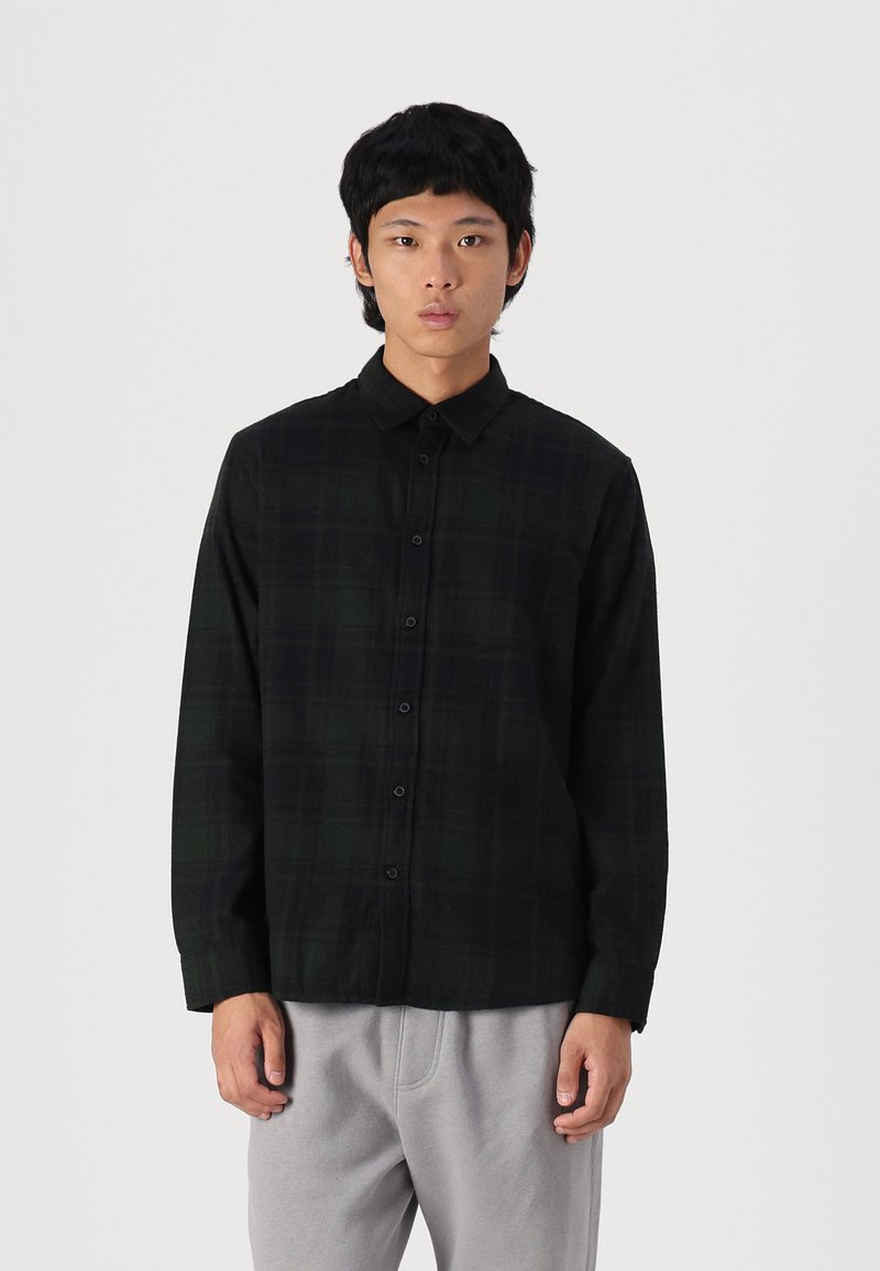 Long-sleeve, button-up shirt in dark green plaid fabric. Features a collar, front buttons, and a relaxed fit. Soft texture, minimal design.