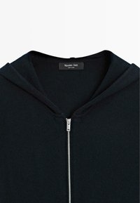 Dunkelblaues Zip-Hoodie aus einem strukturierten Stoff, mit Kapuze und einem silbernen Reißverschluss. Das Markenlabel ist im Kragen sichtbar.