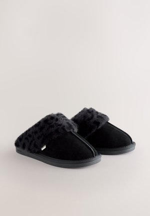 Pantofole in suede nero con una morbida tomaia in pelliccia sintetica nera con stampa leopardata e suola piatta in gomma, caratterizzate da una cucitura lungo la parte anteriore.