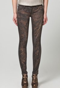 Mörkbruna skinny jeans med en ruggad textur, framfickor och kontrasterande sömmar, tillsammans med bronsfärgade högklackade skor.