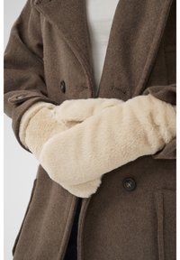 Person wearing beige faux fur mittens crossed over a brown wool coat with black buttons.